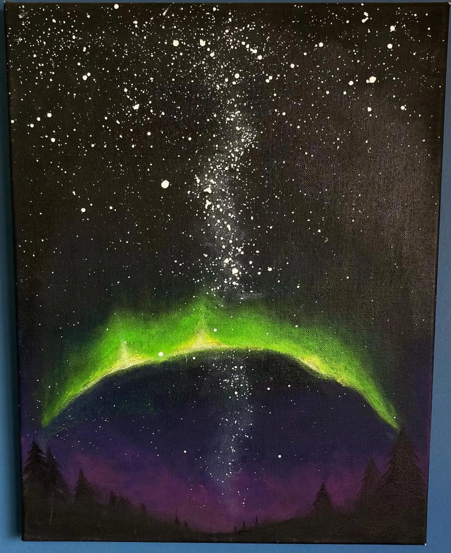 Aurora. A green and purple aurora arcing over a dark treeline.